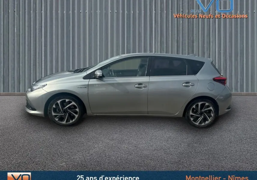 Profil côté gauche d'une Toyota Auris Business Hybride gris clair avec jantes alliage 17 pouces sur fond urbain.