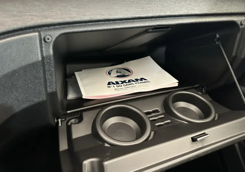 Vue rapprochée de la boîte à gants ouverte de l'AIXAM AMBITION E CITY PACK 2025 avec porte-gobelets intégrés.