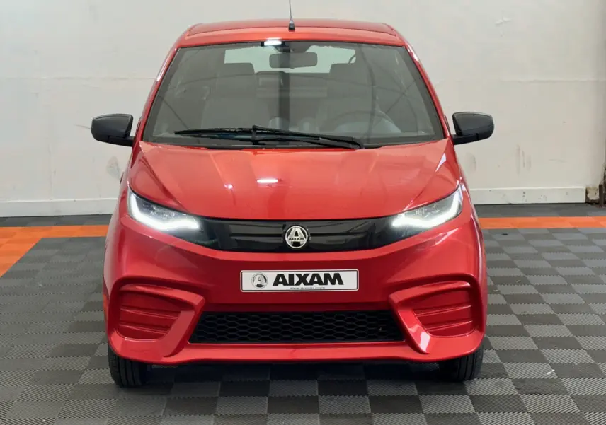 Vue frontale d'une AIXAM AMBITION E CITY PACK rouge 2025 avec phares LED allumés et rétroviseurs noirs.