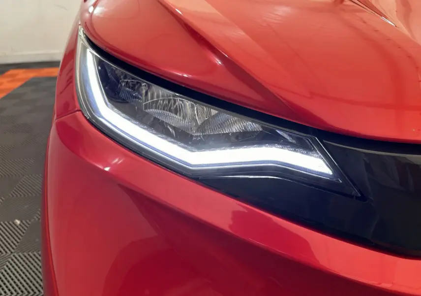 Gros plan sur le phare avant gauche lumineux d'une AIXAM AMBITION E CITY PACK rouge électrique 2025.