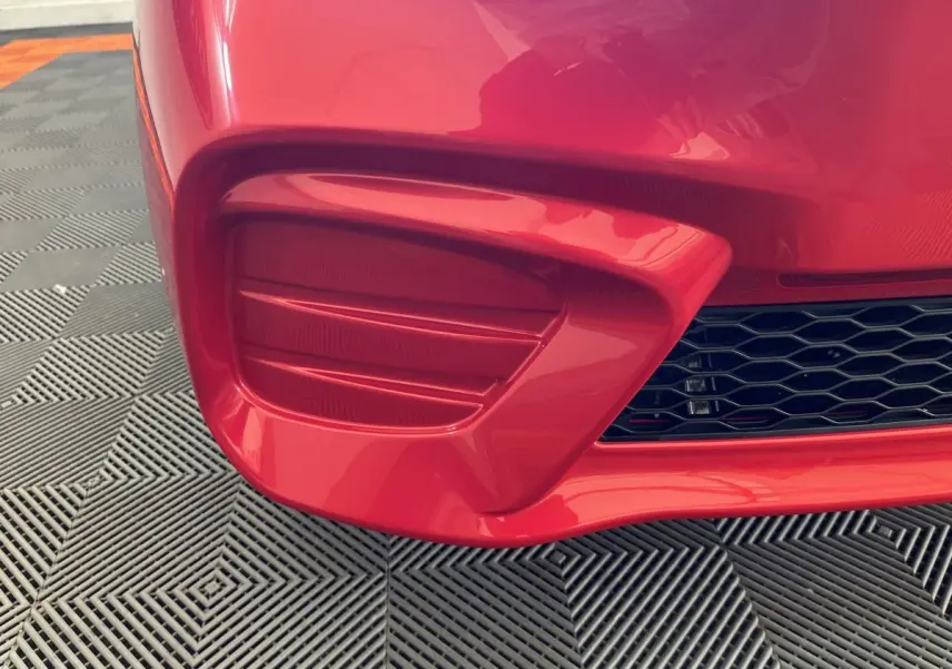 Gros plan sur la partie avant gauche rouge de l'AIXAM AMBITION E CITY PACK 2025 avec prise d'air et grille noire.