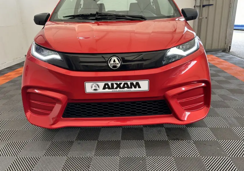 Vue frontale d'une Aixam Ambition E City Pack rouge 2025 avec calandre noire et phares LED allumés.