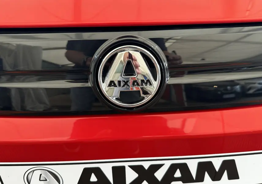 Gros plan sur le logo chromé AIXAM sur la calandre rouge vif de la microcar électrique 2025 Ambition E City Pack.