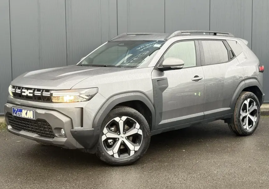 Vue 3/4 avant d'un Dacia Duster 2026 gris schiste avec jantes alliage et barres de toit noires.