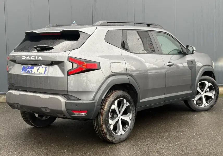 Vue 3/4 arrière droit d'un Dacia Duster gris schiste avec jantes alliage diamantées et barres de toit noires.