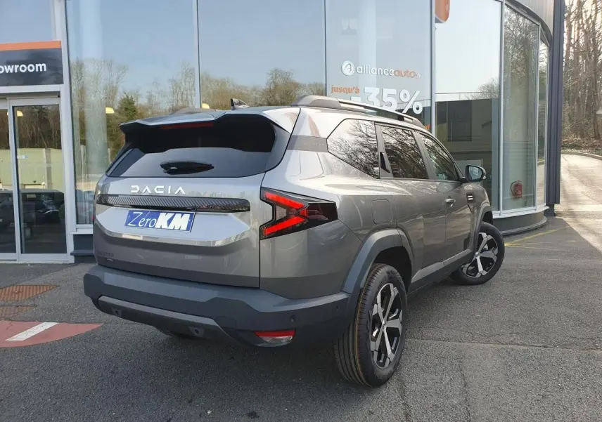 Vue 3/4 arrière droite du Dacia Bigster gris schiste avec jantes alliage 18 pouces et barres de toit longitudinales.