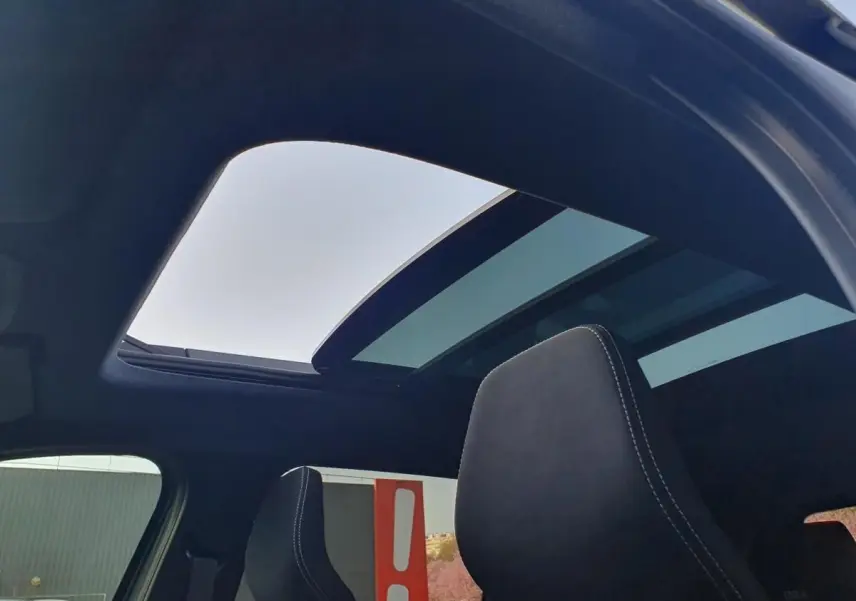 Vue intérieure du toit panoramique ouvert du Dacia Bigster gris schiste, avec appuie-tête avant en tissu noir.