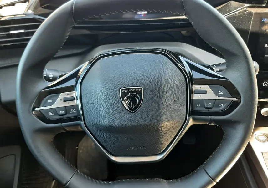 Vue rapprochée du volant noir du Peugeot 308 SW Hybrid 145ch 2025, avec commandes intégrées et logo lion central.
