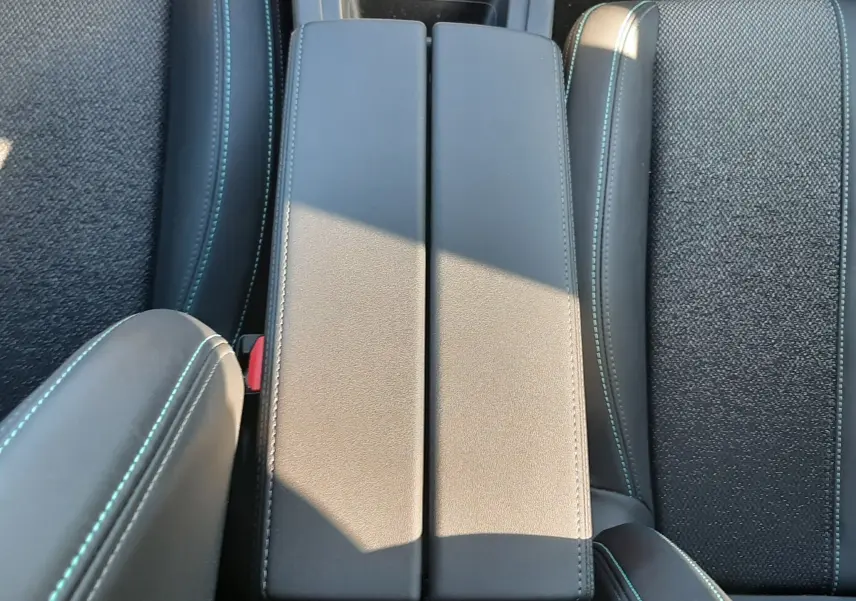 Vue plongeante sur l'accoudoir central en cuir gris avec surpiqûres bleues, entouré de sièges tissu gris du Peugeot 308 SW Hybrid 2025.