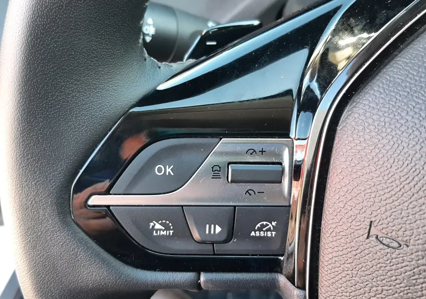 Gros plan sur les commandes au volant côté gauche de la Peugeot 308 SW Hybrid 2025, finition noire brillante.