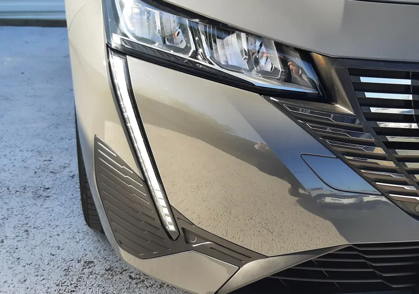 Gros plan sur l'avant droit gris selenium métallisé du Peugeot 308 SW Hybrid 2025, mettant en valeur le phare et la calandre.