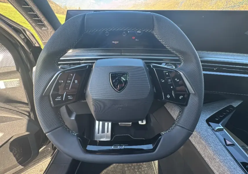Vue rapprochée du volant cuir multifonctions Peugeot 3008 GT noir avec logo et pédalier aluminium visible.
