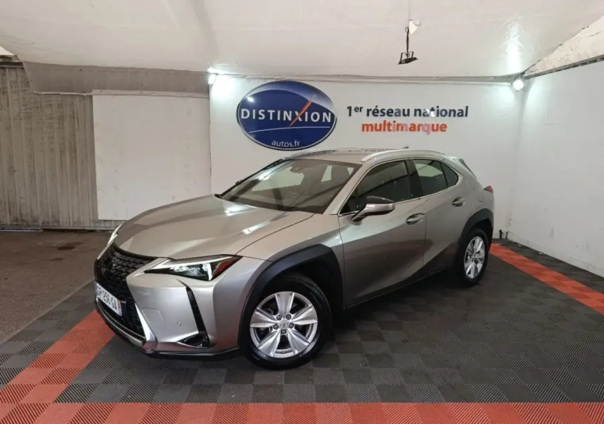 Lexus UX 250H gris clair en 3/4 avant droit, avec jantes alliage et protections noires autour des roues.