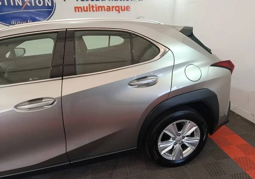 Vue côté droit arrière d’un Lexus UX 250H gris clair avec jante alliage et spoiler de toit visible.