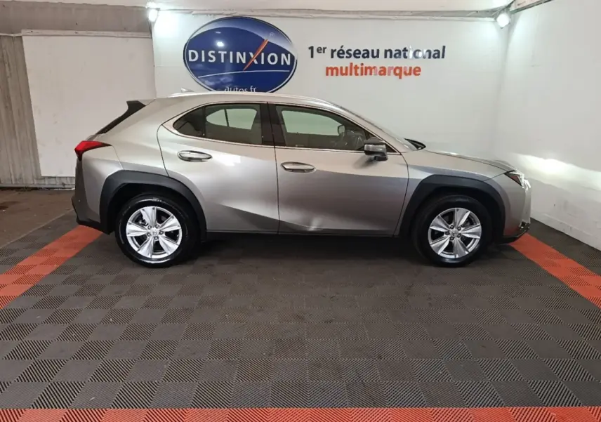 Profil côté gauche d’un Lexus UX 250H gris clair stationné en intérieur avec jantes alliage et protections noires.