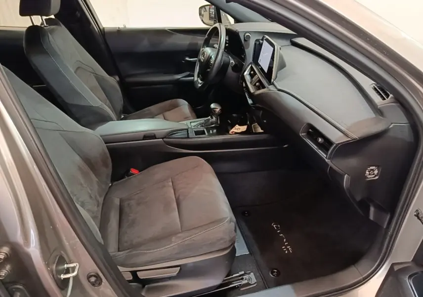 Vue intérieure côté conducteur du Lexus UX 250H gris clair, montrant sièges en tissu et tableau de bord avec écran tactile.