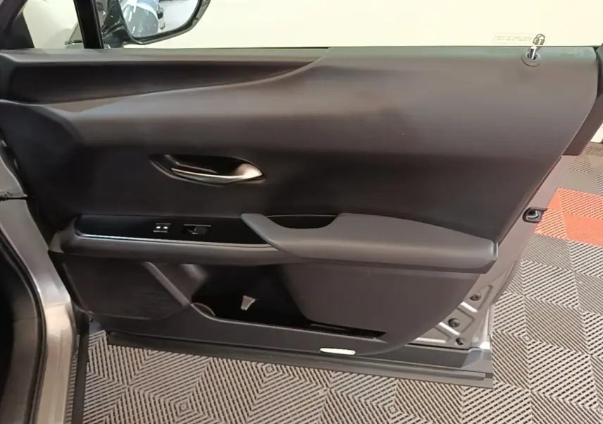 Vue intérieure de la porte avant gauche d’un Lexus UX 250H gris clair, avec commandes électriques et poignée intégrée.