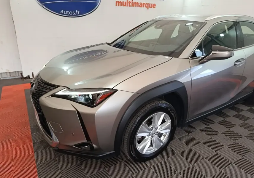 Lexus UX 250H gris clair en 3/4 avant droit, avec calandre noire distinctive et jantes argentées.