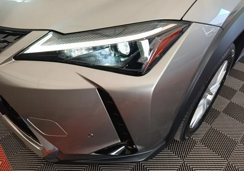 Gros plan sur l’avant droit gris clair du Lexus UX 250H 2WD avec phare LED et partie de la roue visible.