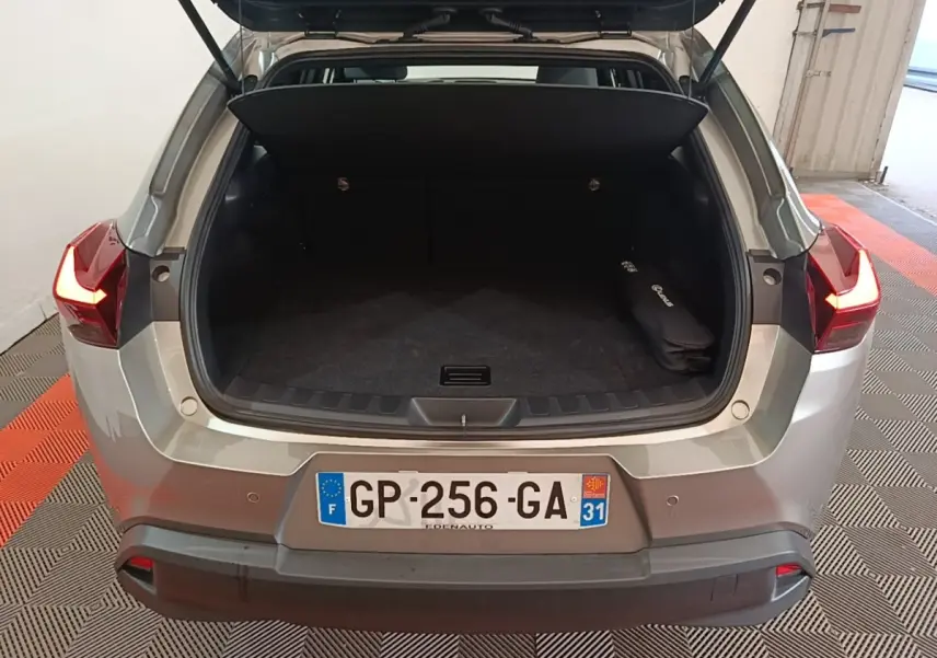 Vue arrière ouverte du coffre d'un Lexus UX 250H gris clair avec feux arrière allumés dans un garage.