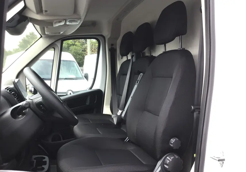 Vue intérieure côté conducteur du Peugeot Boxer Fourgon blanc 2025, montrant les trois sièges noirs et le volant.
