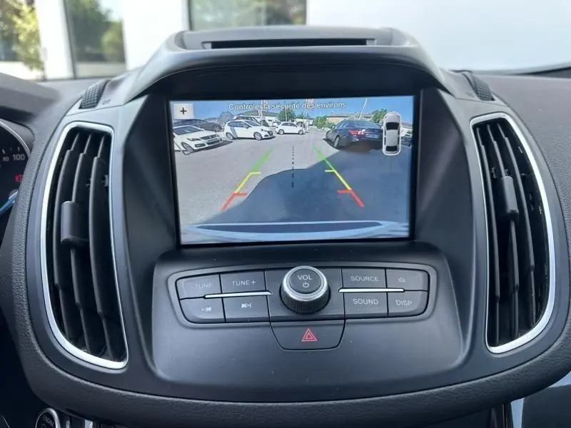 Écran central du Ford C-MAX 2017 affichant la caméra de recul avec vue arrière du parking et voitures blanches visibles.