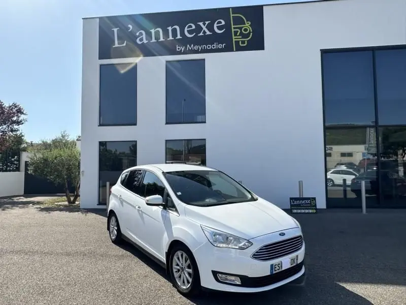 Ford C-MAX blanc en 3/4 avant droit, version Titanium 2017, garé devant un bâtiment moderne blanc.