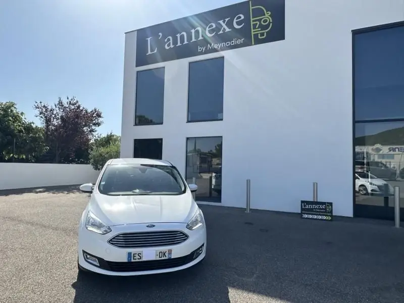 Vue de face d'une Ford C-MAX blanc 2017 garée devant un bâtiment moderne avec enseigne L'annexe.
