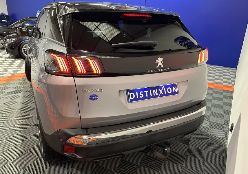 Vue 3/4 arrière d’un Peugeot 3008 gris Artense avec toit noir, feux allumés et attelage visible.