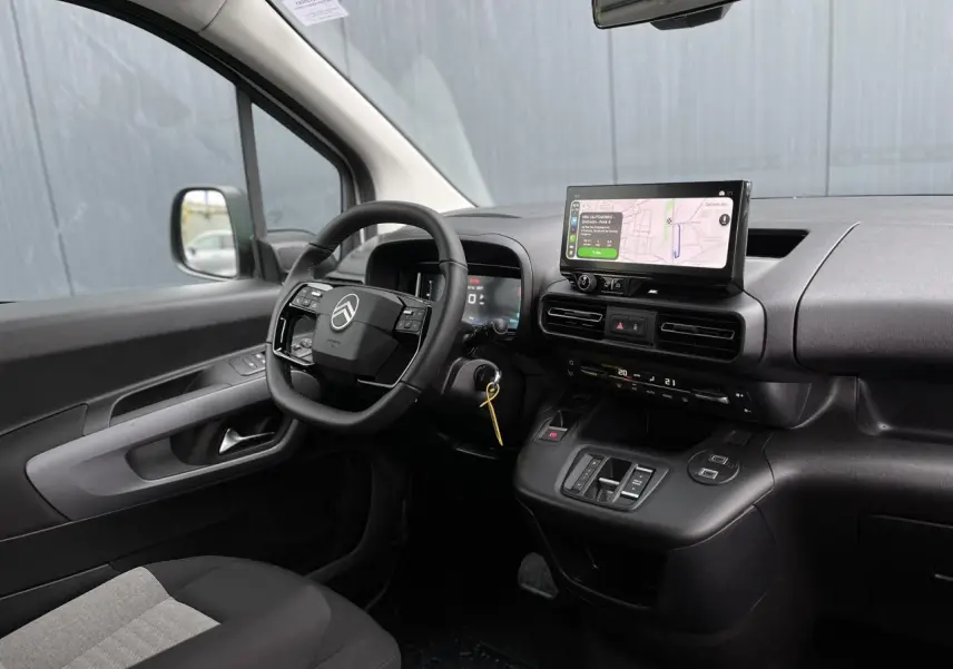 Vue intérieure côté conducteur du Citroën Berlingo blanc, volant multifonctions et écran tactile avec navigation visible.
