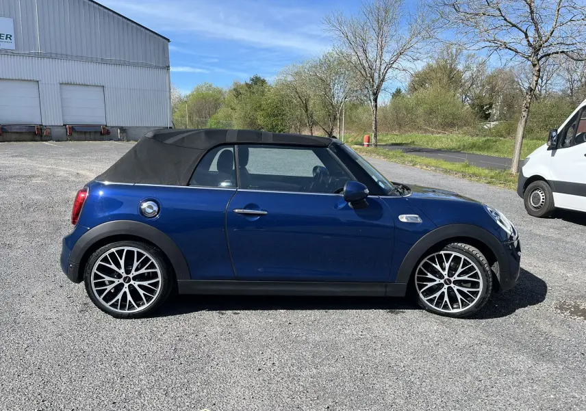 Vue de profil côté gauche d'une MINI Cabriolet F57 Cooper S bleu avec capote noire fermée et jantes alliage bicolores.