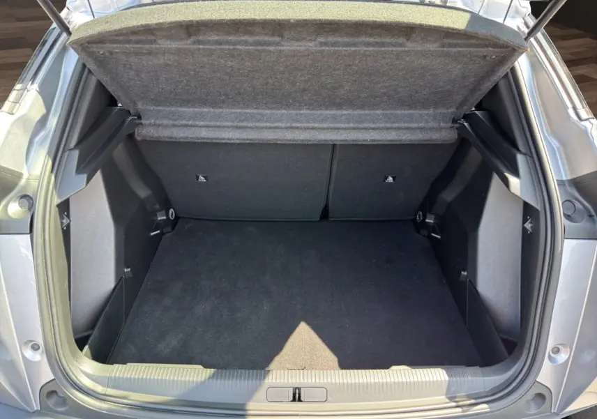 Coffre ouvert vu de l'arrière d'un Peugeot 2008 Hybrid 145 gris clair, montrant un espace de chargement propre et spacieux.