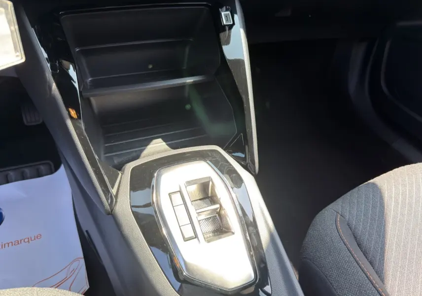 Gros plan sur la console centrale noire brillante et le levier de vitesses automatique dans l’habitacle du Peugeot 2008 gris clair.