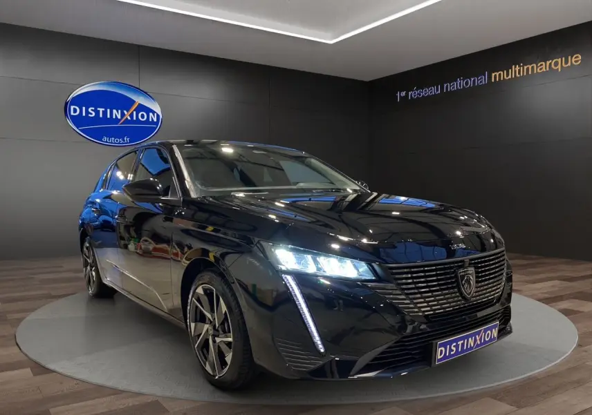 Peugeot 308 noir Perla Nera vue 3/4 avant droit avec phares LED allumés en showroom.