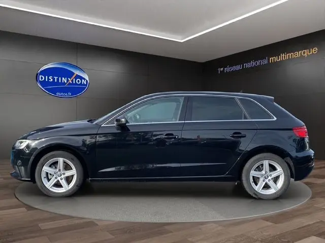 Profil côté gauche d'une Audi A3 Sportback noire 5 portes avec jantes alliage 16 pouces en présentation showroom.