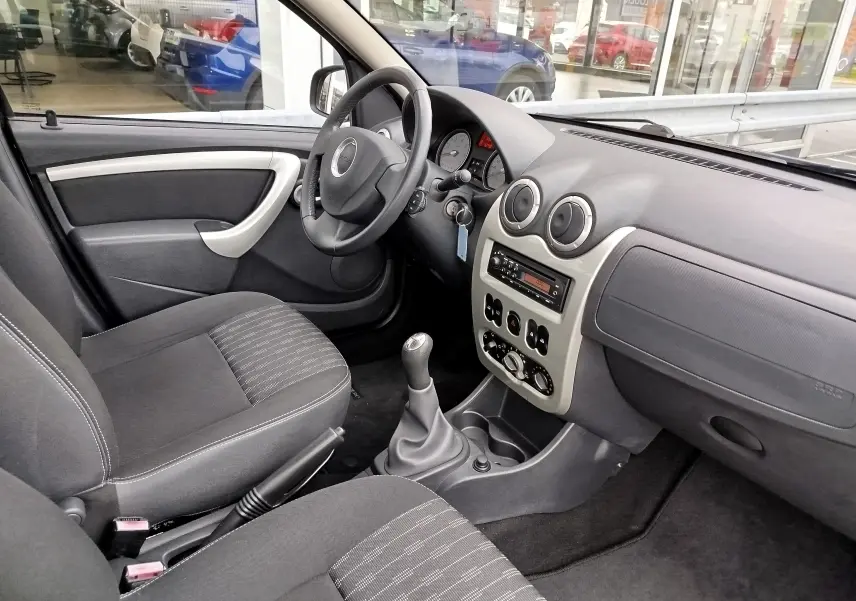 Vue intérieure côté conducteur de la Dacia Sandero 2011 avec tableau de bord gris, volant cuir et sièges tissu gris foncé.