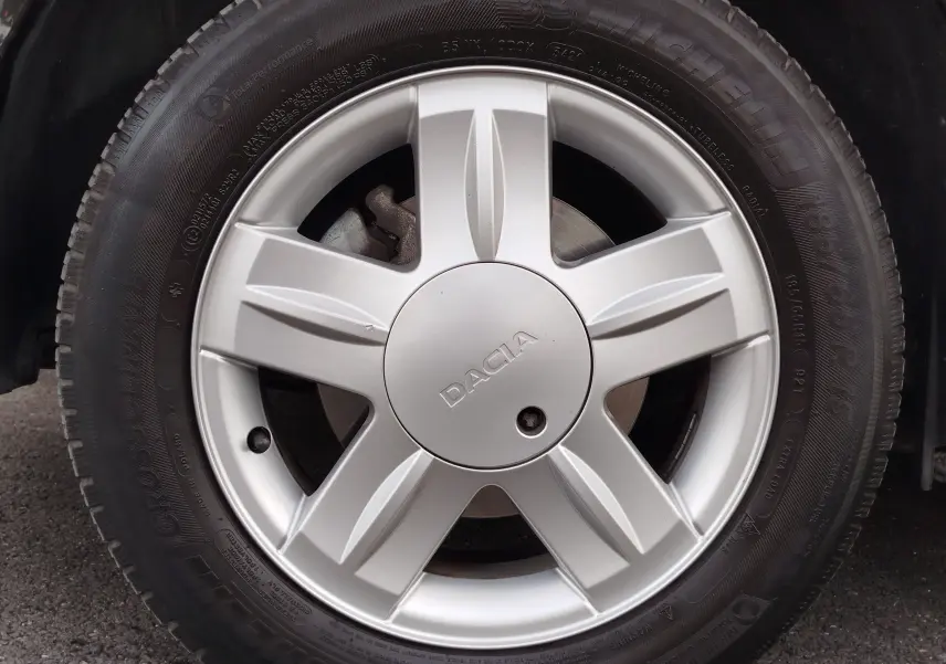 Gros plan sur la roue avant gauche de la Dacia Sandero noire, avec jante argentée et logo central DACIA visible.