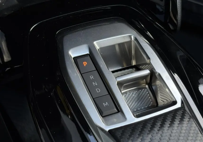 Gros plan sur la console centrale noire brillante du Peugeot 2008 Hybrid 145 avec sélecteur de boîte automatique.