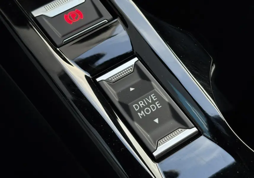 Gros plan sur la console centrale noire brillante du Peugeot 2008 Hybrid 145 avec bouton Drive Mode et frein de stationnement électrique.