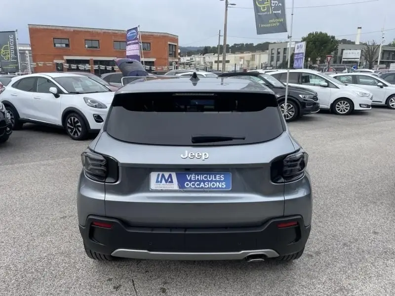Vue arrière d'un Jeep Avenger gris métal 2025, avec vitres teintées et feux arrière fumés, sur parking extérieur.