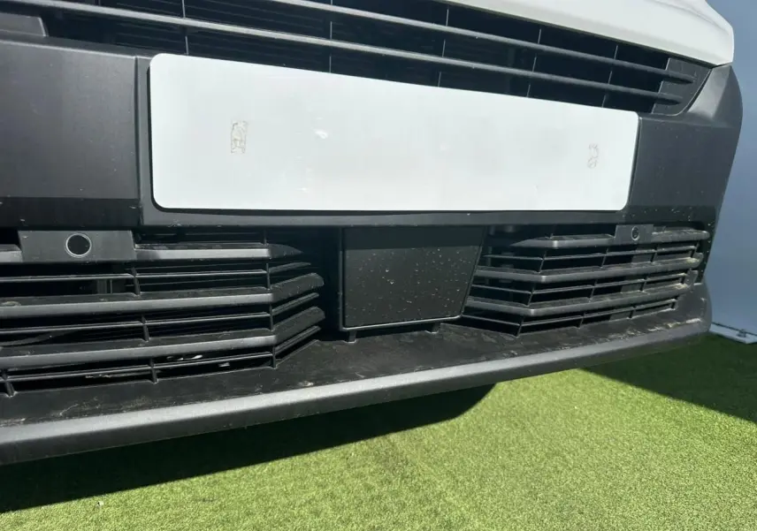 Gros plan sur la calandre avant noire et la plaque blanche du Citroën Berlingo III blanc Icy, vue de face basse.