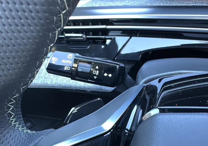 Gros plan sur la commande des feux et clignotants côté gauche du volant cuir perforé du Peugeot 3008 blanc okénite.
