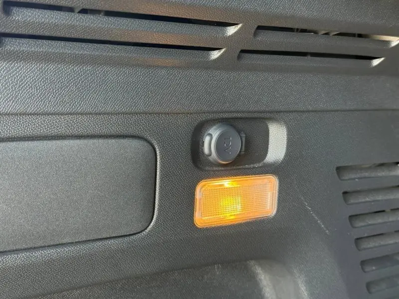 Détail intérieur du coffre du Peugeot 3008 Hybride Rechargeable noir, montrant une prise 12V et une lampe orange allumée.