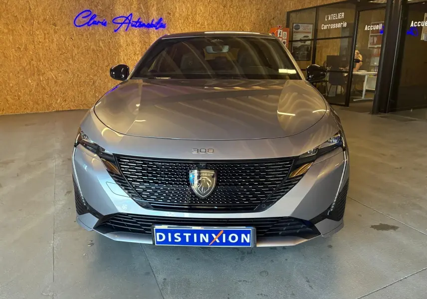 Vue de face d'une Peugeot 308 gris métallisé 2025 avec calandre noire et logo lion distinctif, en intérieur showroom.