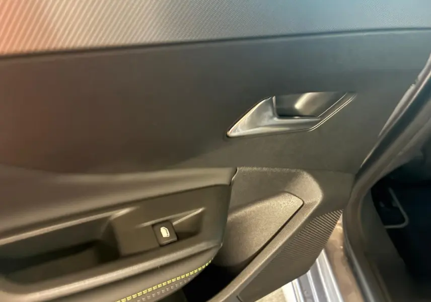 Détail de la porte intérieure côté gauche d'une Peugeot 308 gris, montrant la poignée et le bouton de verrouillage.