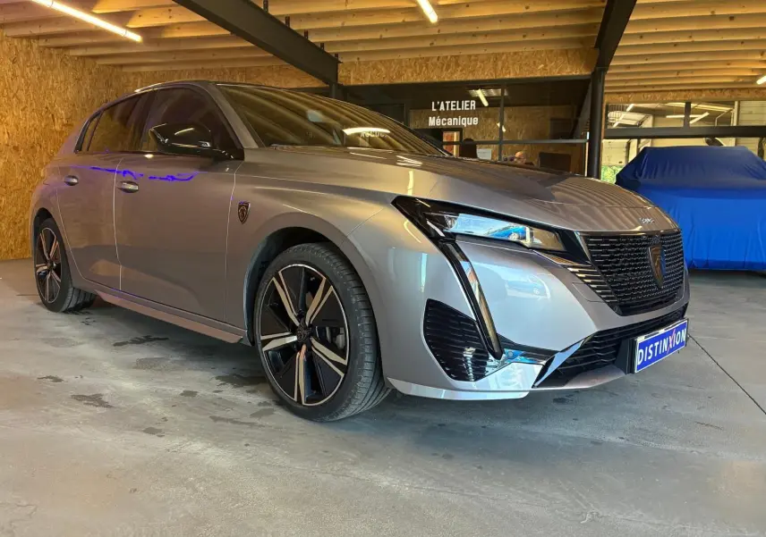 Peugeot 308 1.2 Hybrid gris vue 3/4 avant droit, avec jantes noires et calandre au design moderne dans un atelier.