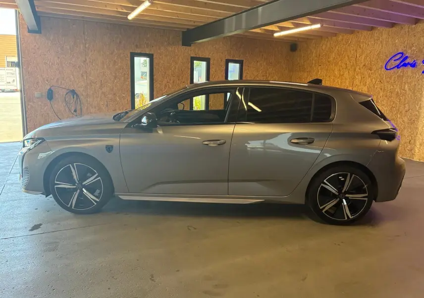 Peugeot 308 1.2 Hybrid gris vue de profil côté gauche, avec jantes noires et toit noir en intérieur d'atelier.