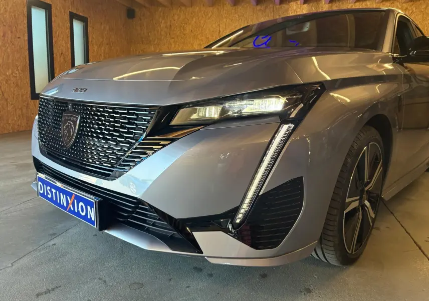 Vue 3/4 avant droit d'une Peugeot 308 gris métallisé avec calandre noire et feux LED distinctifs, en intérieur.
