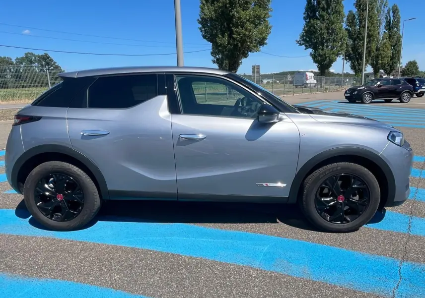 Vue latérale côté gauche d'un DS3 Crossback Performance Line gris métallisé avec jantes noires sur un parking.