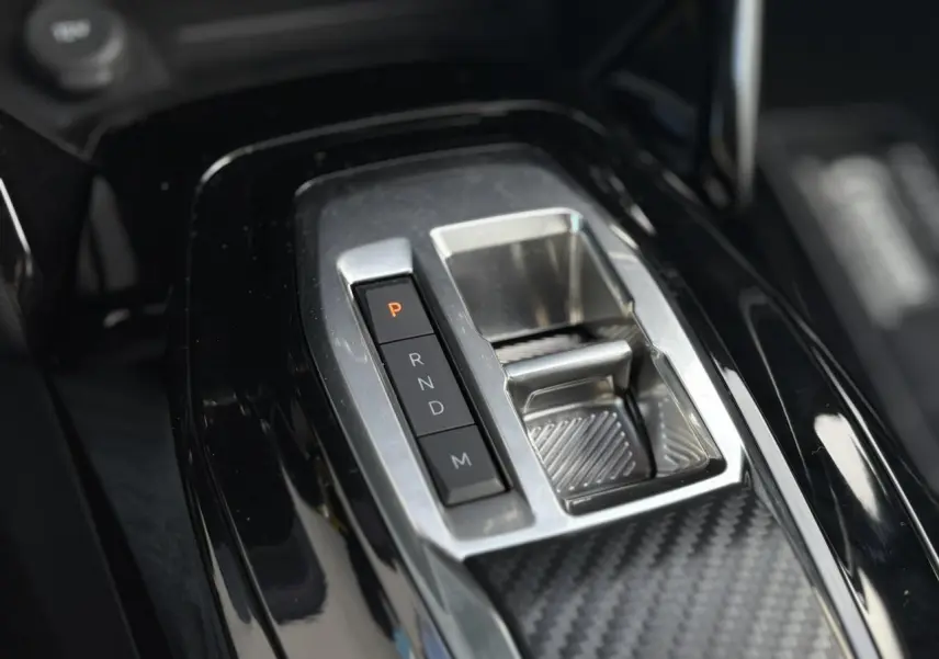 Gros plan sur la console centrale noire brillante du Peugeot 2008 Hybrid 145 avec sélecteur de boîte automatique.